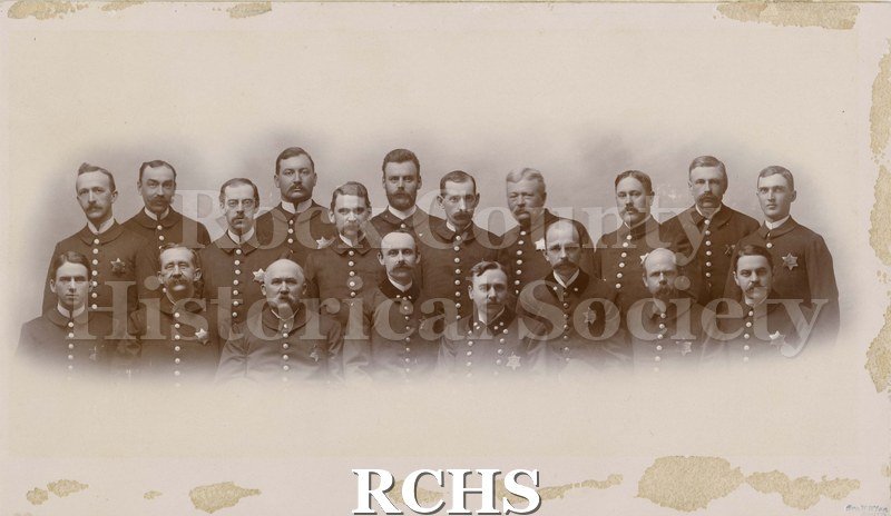 Black and white photograph of "Fire Police Janesville Wisconsin 1895." Shows 19 men in uniform. Bottom Row: W. P Sayles 4th from left E.G.F.