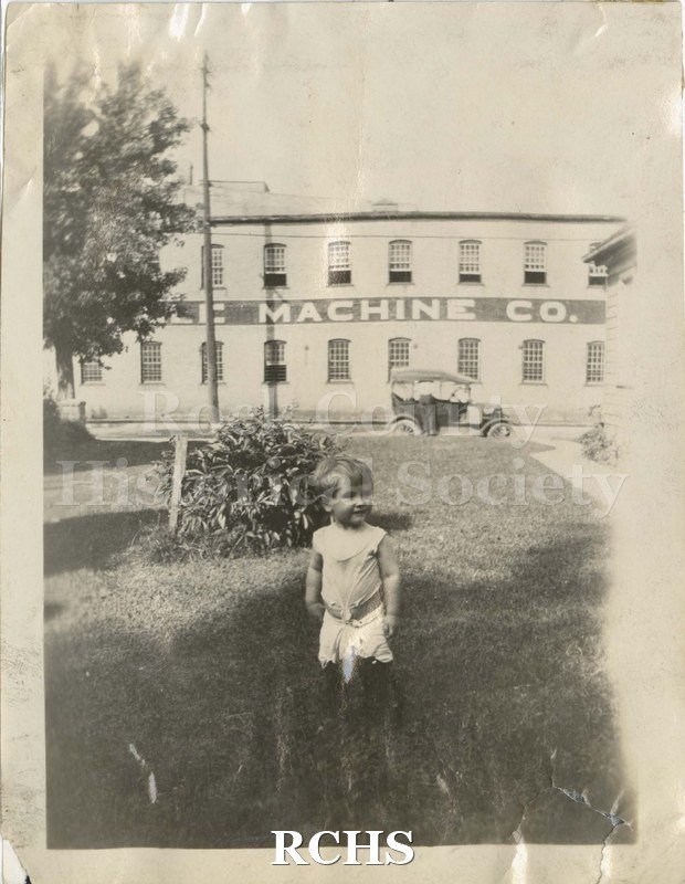 Black and white photograph of Janesville Machine Co. There is a child standing in front of Janesville Machine Co.