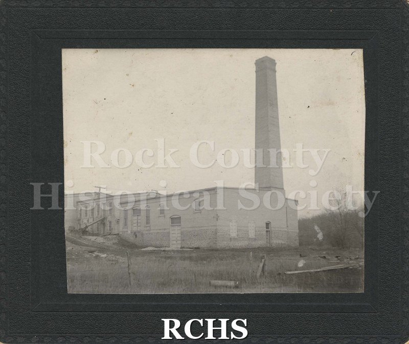 Black and white photograph of a Power Plant. An unidentified power plant is shown with a smokestack-Janesville?. Building is surrounded by grass.