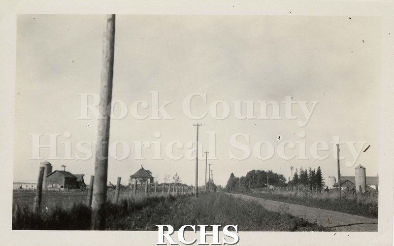 Black and white photograph of rural electrification. There is a rural road showing electrical poles.