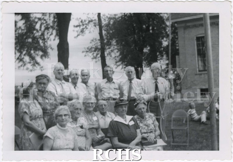 Black and white photograph of West Center First School Reunion. Shows older men and women sitting and standing outdoors in formal dress.