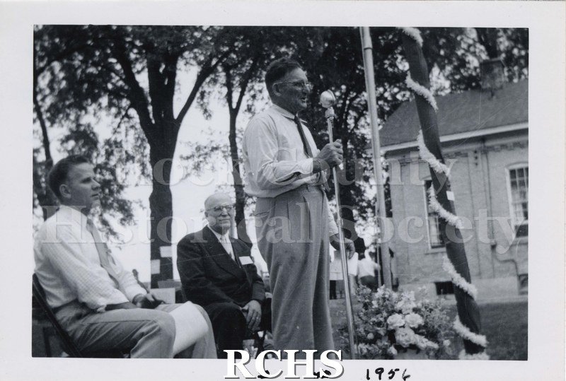 Black and white photograph of Raymond Snyder speaking at a microphone at the 1st reunion at West Center School.