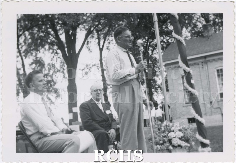 Black and white photograph of Raymond Snyder speaking at a microphone at the 1st reunion at West Center School.