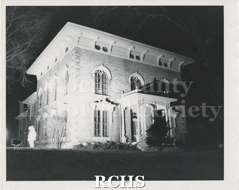 Black and white photograph of the Tallman House at night. Seems to be spotlighted. Shows person silhouetted on left side.