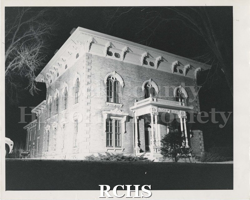 Black and white photograph of the Tallman House at night. Seems to be spotlighted. Shows person silhouetted on left side.