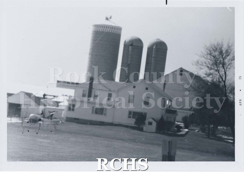 Black and white photograph of the Newark, Joranlien-Haugen farm house and farm buildings behind, including three silos. "APR. 75" written along one side.