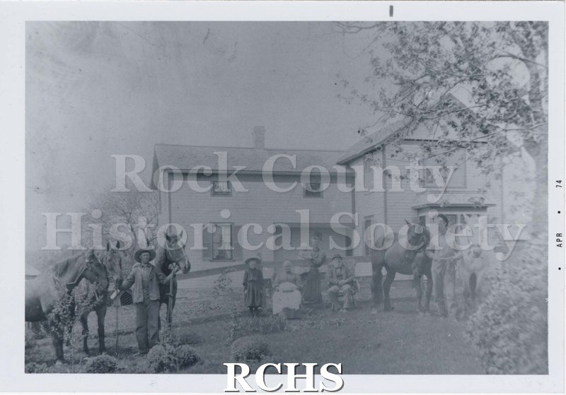 Black and white photograph of the Newark Engan-Mahlum farm, 1870's. Shows a family sitting and standing outside their house, circa 1870s.