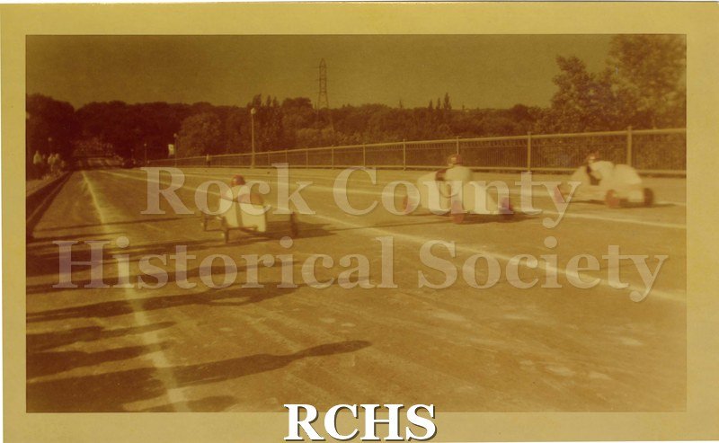 Tinted photo of soap box cars racing at the Janesville Soap Box Derby, 1948. Carliss B. Shuler's car is the one on the left.