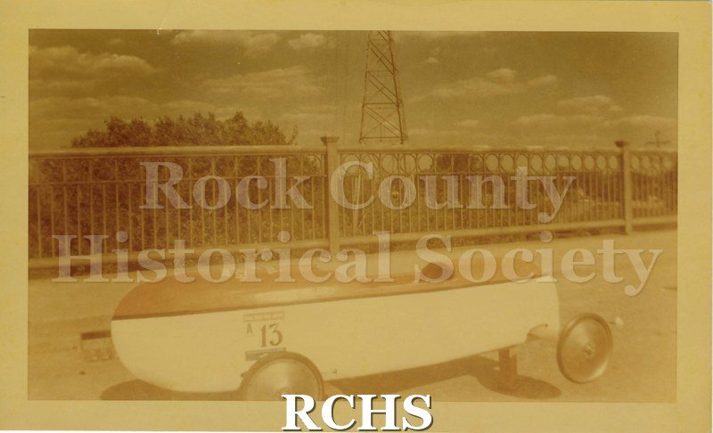 Tinted photo of Carliss B. Shuler's soap box car siting empty on Monterey Bridge. Part of the Janesville Soap Box Derby, 1948.