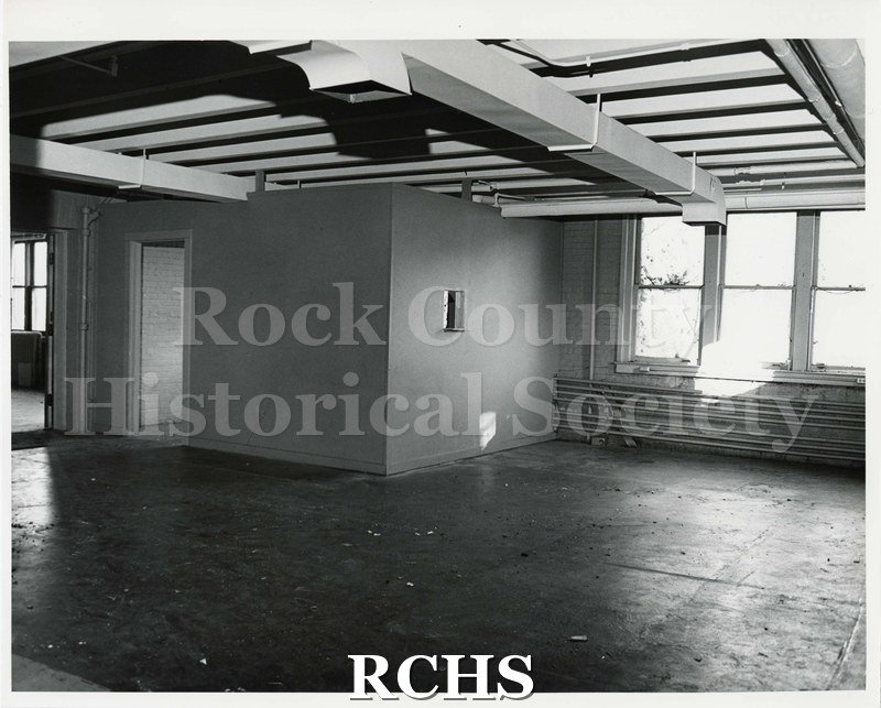 Black and white photograph of an empty room in Pearson's Hall. There are two doors leading out of frame on the left hand side of the image.