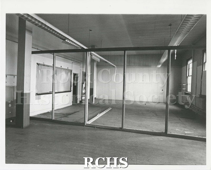 Black and white photograph of Pearson's Hall Interior before renovation. Empty room, stairs visible at back, chalk board, wooden frame partitions.