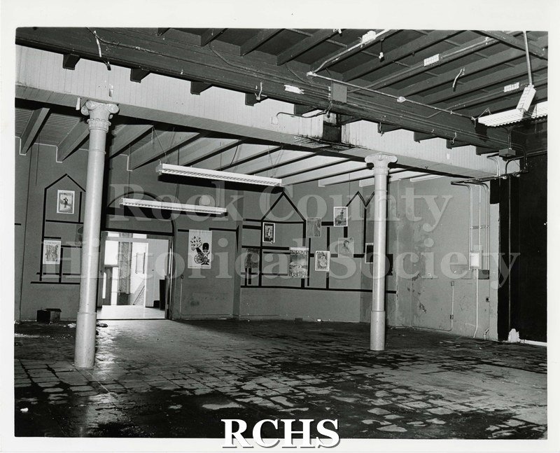 Black and white photograph of Pearson's Hall Interior before renovation. Room with two white pillars and various posters on the back wall.