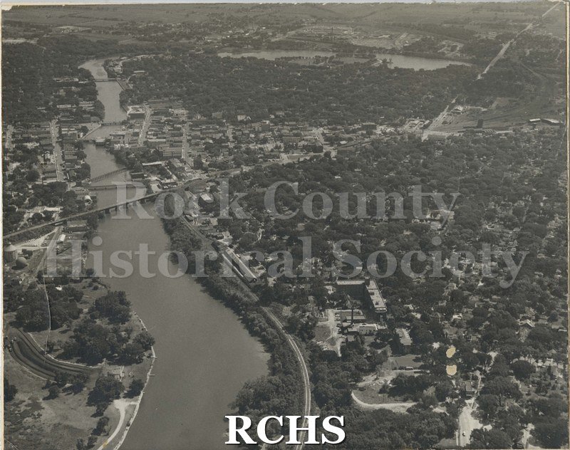 Black and white photograph of an aerial view of Janesville. The Rock River is displayed prominently and bends toward the right in the back of the image.