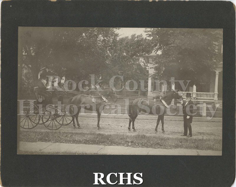 Black and white photograph of George McKey dressed as Cols. Nonesuch, circa 1910. One man with a long white beard, rides in a black buggy drawn by two horses.