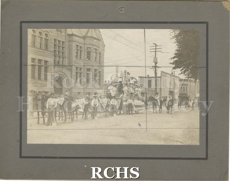 Black and white photograph of the "W.J. Hilt, Riverside Cement Blocks" float. Six horses draw the float, while many women and men ride it.