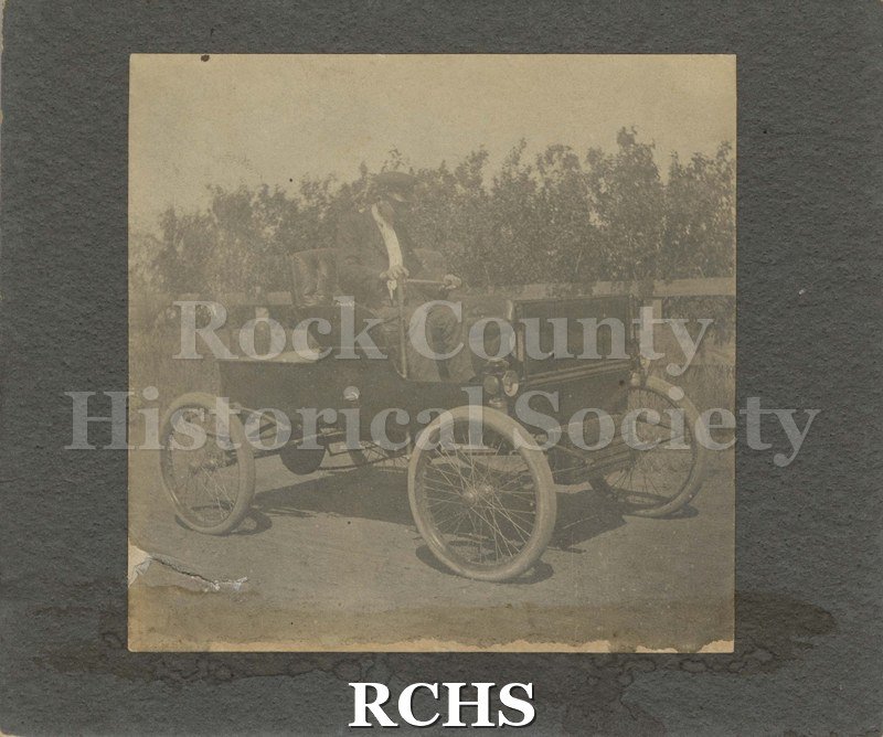 Black and white photograph of the Remington auto. Has two large wheels in front and two smaller wheels in back. There is no cab.