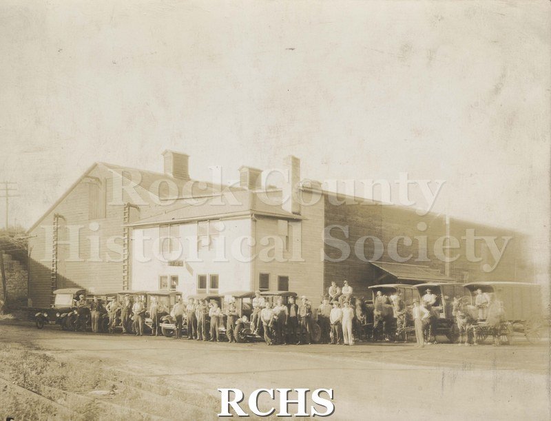 Black and white photograph of City Ice Co. 1930. Shows a building with men standing in front of several cars and three wagons pulled by a team of horses.