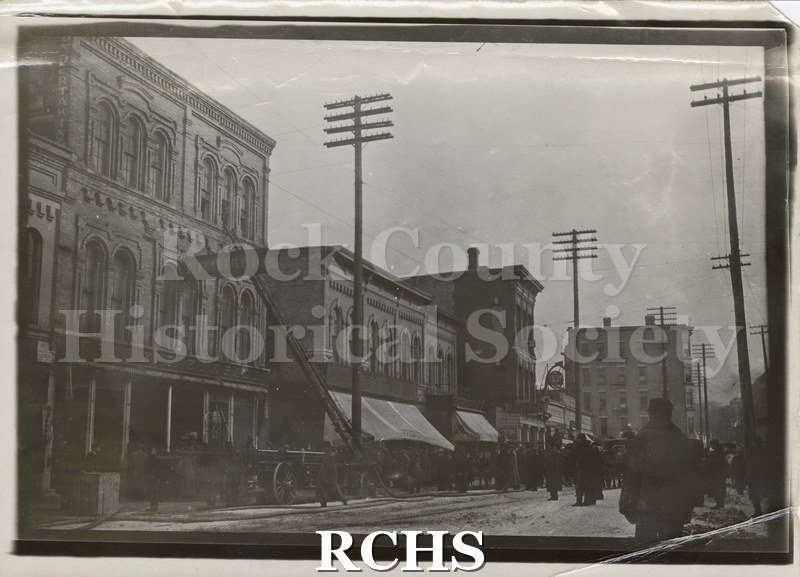 Black and white photograph of Kimball Furniture Store Fire 1911. Shows three story building on left with ladder up to third floor.