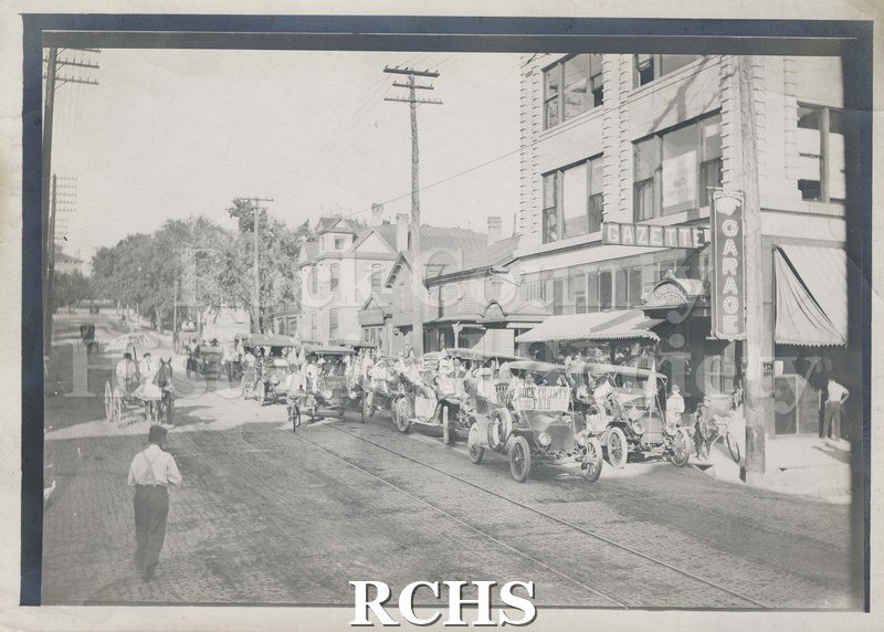 Black and white photograph of vehicle caravan on city street to promote Rock County Fair.