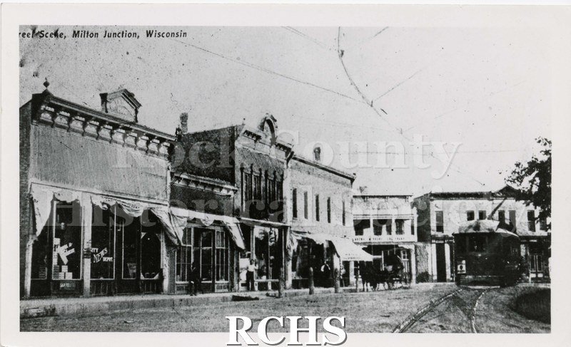 Black and white photograph of Milton Junction, Wisconsin. Shows store fronts and trolley on right side.