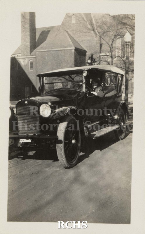 Black and white photograph of a vintage automobile. Shows a man seated in old automobile. Written on reverse: "Back of OLD Methodist Church Court & Franklin St.".