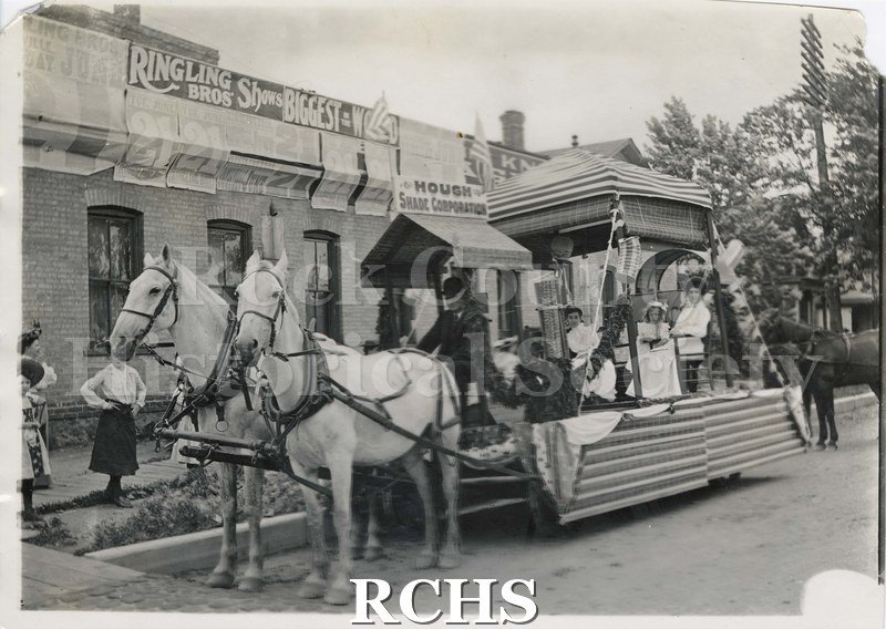 Black and white photograph of a horse-drawn parade float for Hough Shade Corporation. Building in background appears to be Hough Corp.