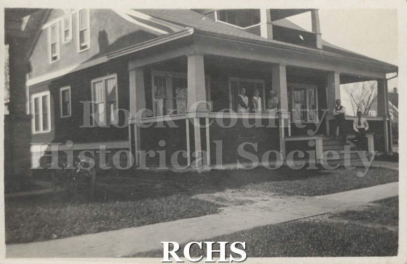 Black and white photograph of a house at 1066 Union St., Janesville, WI. Shows a two story house with a porch in front and two people on the porch.