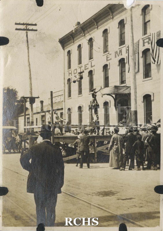 Black and white photograph of an acrobatic event on platform in front of Hotel Empire, Milwaukee Street, Janesville.