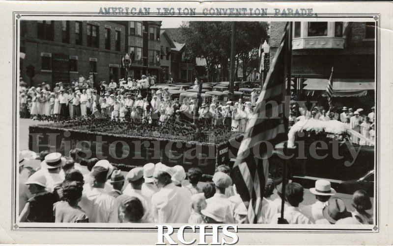 Black and white photograph of the American Legion Convention Parade in downtown Janesville. Truck is pulling a parade float commemorating Flanders Field.