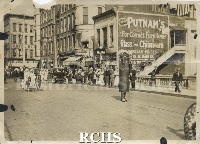 Black and white photograph of a parade on W. Milwaukee St., Janesville, crossing bridge.