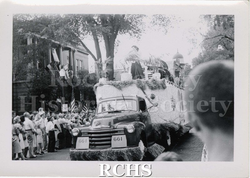 Black and white photograph of a parade float in front of Carnegie Library, Main Street, Janesville. Written on reverse: "c. 1941".