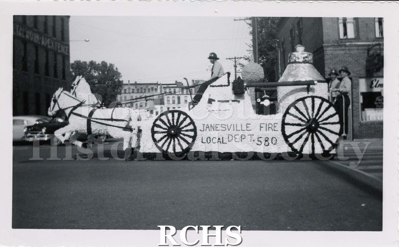 Black and white photograph of the Janesville Fire Department Parade Float. Same float as 2008.33.55. Side view of float. "JANESVILLE FIRE/LOCAL DEPT 580".