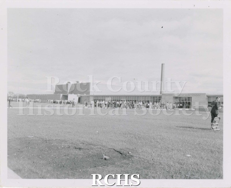 Black and white photograph of Janesville Senior High School (Joseph A. Craig). Students are leaving the building.