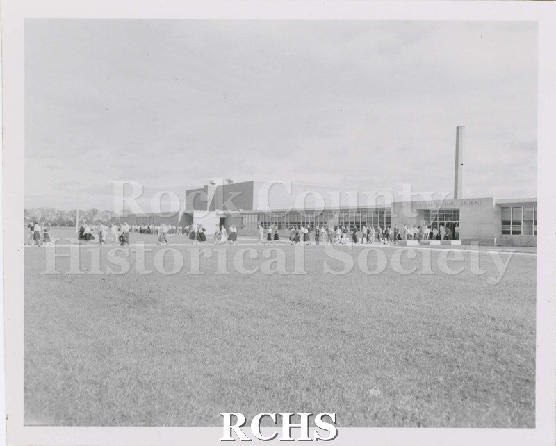 Black and white photograph of Janesville Senior High School (Joseph A. Craig). Students are leaving the building.