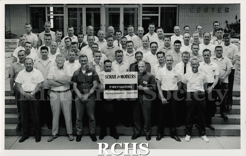 Black and white photograph of School for Workers Firefighters. Shows men standing outside of a building.