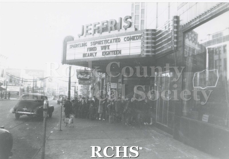 Black and white photograph of Jeffris Theater. Many people are lined up at the doorway. Marquee reads: "Sparkling Sophisticated Comedy Fired Wife Nearly Eighteen".