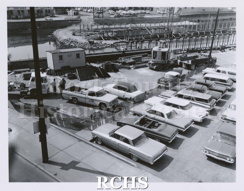 Black and white photograph of parking lot in back of J. C. Penney Company. Shows construction of parking plaza with construction vehicles in foreground.
