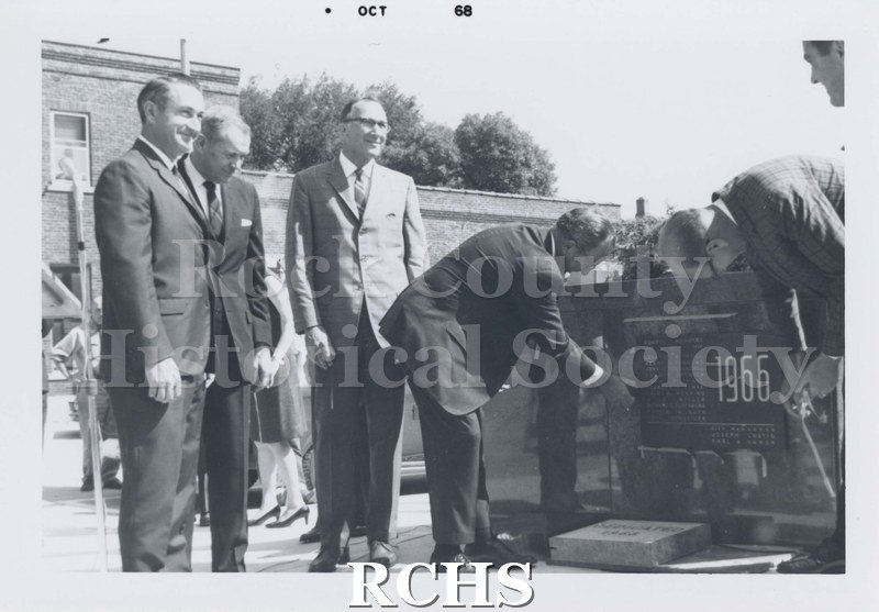 Black and white photograph of five unidentified men standing beside the dedication plaque that reads 1966.