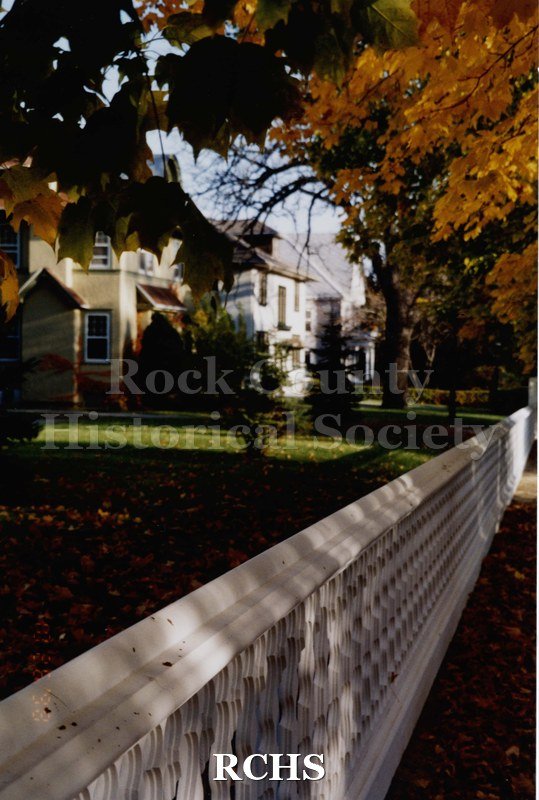 Colored photograph of the front of the Tallman House, looking towards the archives building (the Charles Tallman House). Orange, fall leaves on tree.