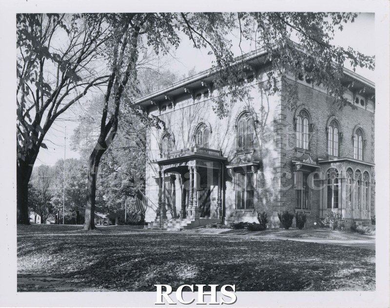 Black and white photograph of the Tallman House taken from road. Shows house from front and east side with trees in front just leafing out.