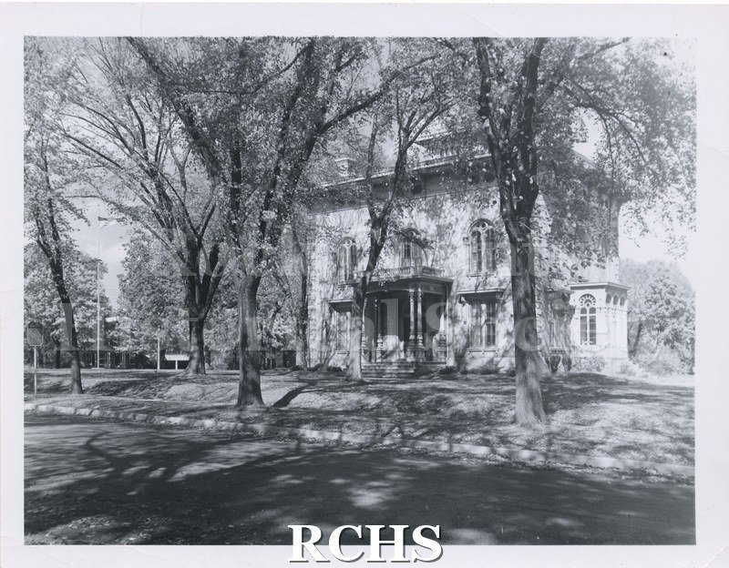 Black and white photograph of the Tallman House taken from road. Shows house from front. Several large trees are in front giving the house a dappled look.