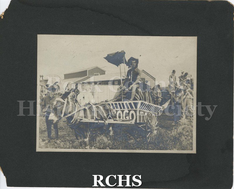 Black and white photograph of a man on mule-driven cart at Nonesuch Brothers Circus with several onlookers. Barn in background.