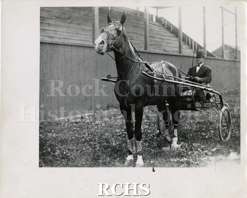 Black and white photograph of a sulky at Rock County Fairgrounds. Shows a two-wheeled sulky with one horse pulling it.