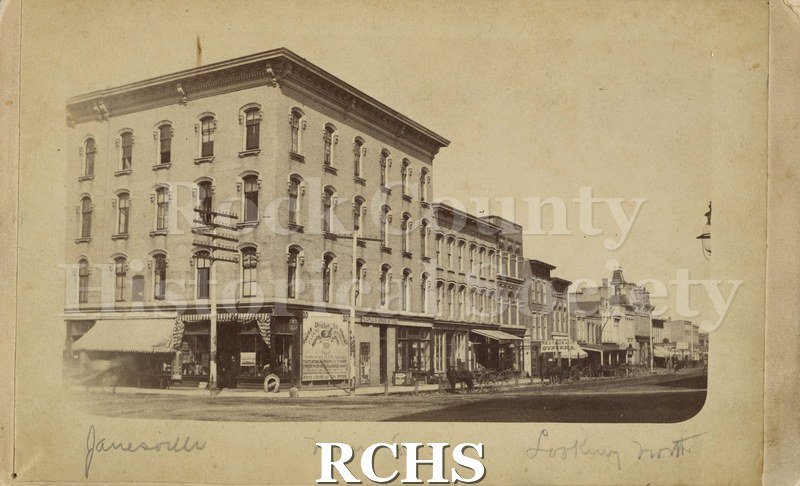 Black and white photograph of Main Street, Janesville, WI, looking north. Shows four story building with People's Drug Store on lower level.