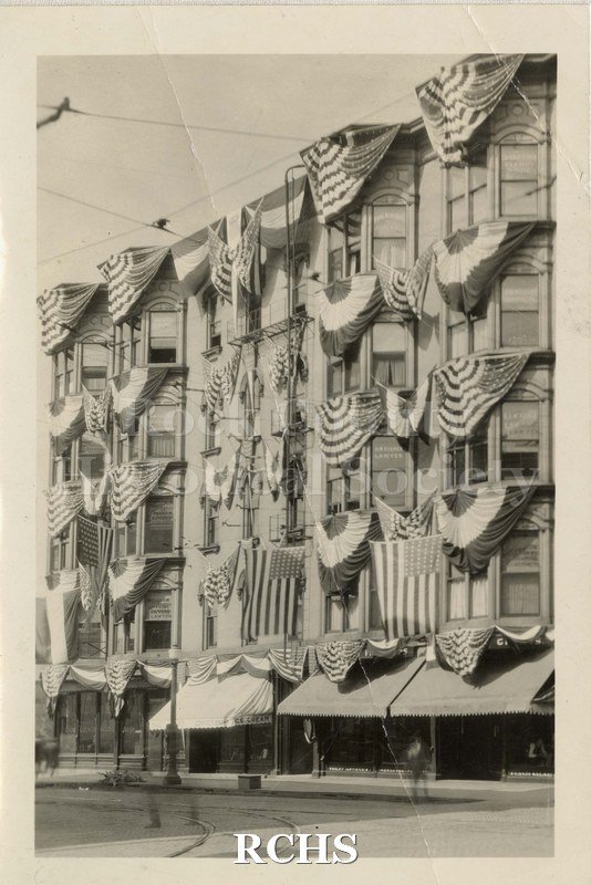 Black and white photograph of Jackman Building Harvest Festival 1924. Shows five story building with patriotic flags and bunting over every window from 2nd to 5th.