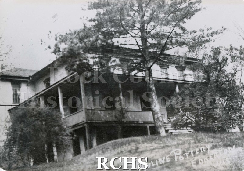 Black and white photograph of the home of Oscar & Pauline Jacobus, Edgergton, WI. House has a large porch surrounding it and a large tree beside the porch steps.
