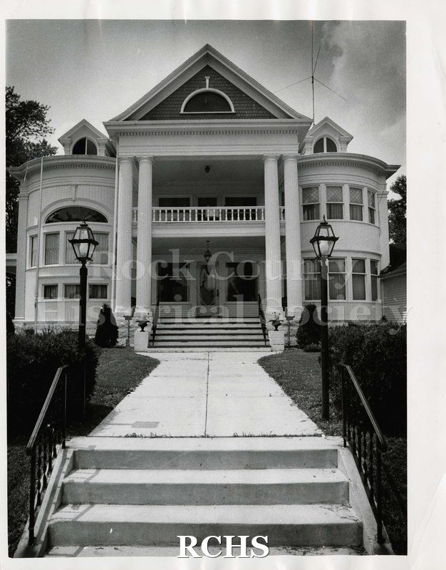 Black and white photograph of Bruni Funeral Home, Edgerton, WI. Shows two story building with four pillars on porch and two lamp posts in front of building.