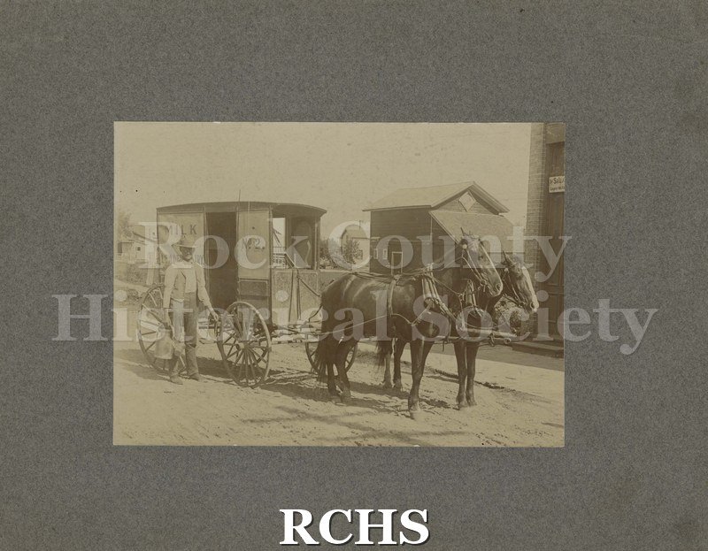 Black and white photograph of an unidentified milkman and wagon on a street (Leader Dairy). Wagon is pulled by two horses. The wagon has a sign: "Milk No. 2" on it.