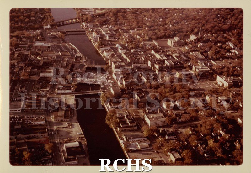 Color photo of Janesville, 1979. Looking North up the Rock River. Dam, bridge, East Milwaukee Street, West Court Street, and West Centerway visible.