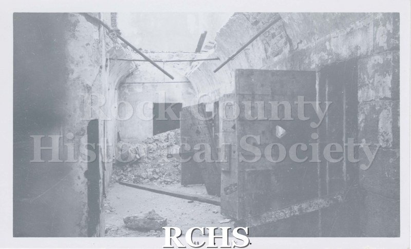 Black and white photograph of the Rock County Jail Demolition. Shows doors; some open and some leaning with debris inside corridor.